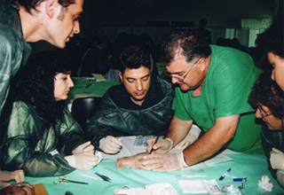 ο Dr. med. B. Παυλιδέλης καθοδηγεί βήμα προς βήμα τους εκπαιδευόμενους συναδέλφους πραγματοποιώντας αφαίρεση σπίλου με απλή συρραφή.